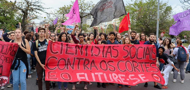Estudantes do curso de Ciências Sociais da UFSC segurando uma faixa vermelha escrita "CIENTISTAS SOCIAIS CONTRA OS CORTES E O FUTURE-SE" no Ato em defesa da Educação, ocorrido no dia três de outubro de dois mil e dezenove.