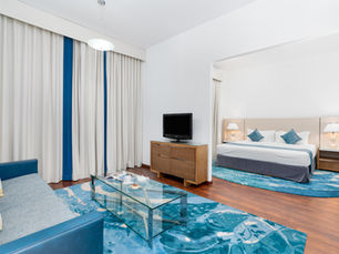 Bright family hotel room with a king-size bed, sofa, seating area and blue décor at Golden Sands Hotel & Residences in Sharjah