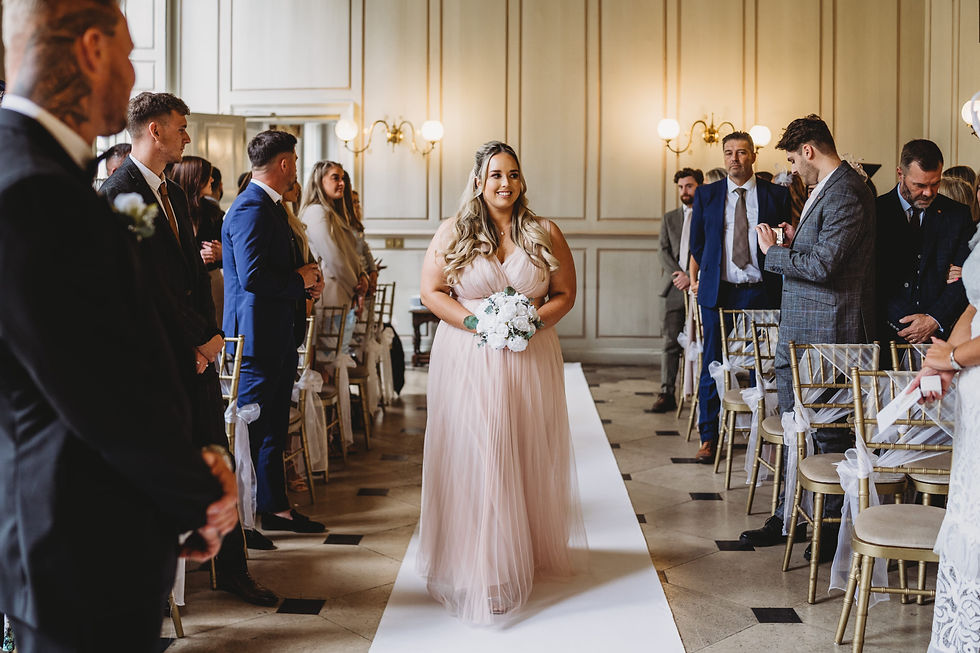 a bridesmaid wearing a pink dress walking down the aisle at gosfield hall
