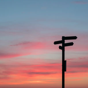 Ein Wegweiser steht vor einem Sonnenuntergang, der den Himmel in rosa und blaue Töne taucht.