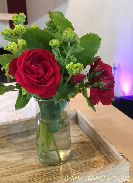 Rote Rosen in Vase auf Holztisch mit grünem Hintergrund.