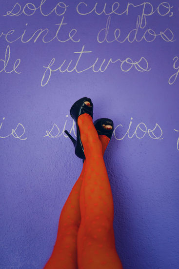 Pies con tacones y medias rojas, texto en pared morada