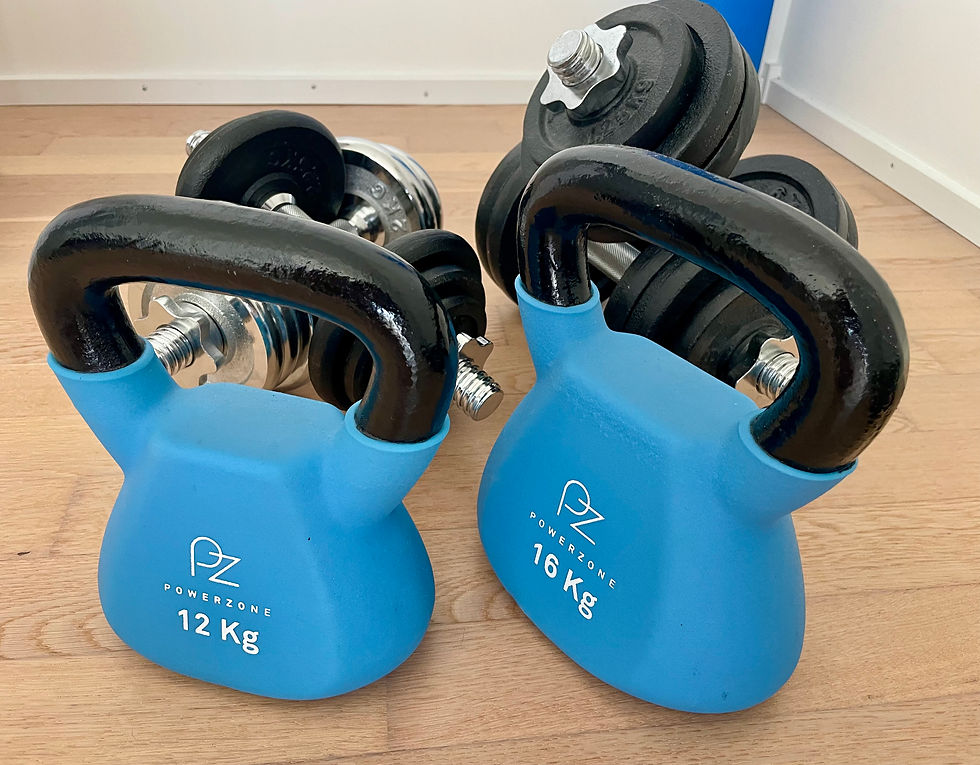 Two blue Powerzone kettlebells, 12 kg and 16 kg, sit on a wooden floor with black dumbbells behind them.