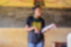 A female Projet Jeune Leader CSE Educator stands in a classroom in rural Madagascar speaking, holding a scripted lesson plan in her hand.