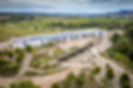 Aerial view of a long narrow white building covered in rooftop solar panels. In the background are vineyards and patches of trees in rural Spain.