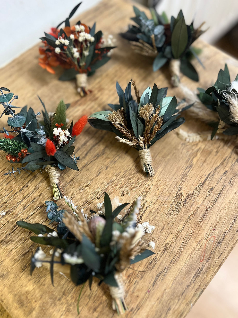 a collection of forest green boutonnières in different designs spread across a wooden table