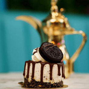 A layered cake decorated with frosting and topped with a chocolate chip cookie