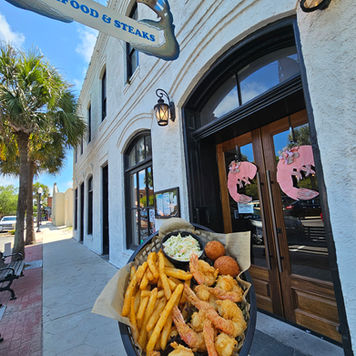 A basket of golden fried shrimp held outside under The Crab Trap sign