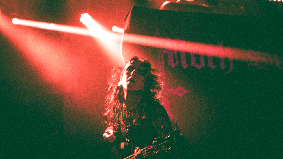 Guitarist in centre, dramatic red lighting bouncing off subjects face. Harsh shadow on right side of image
