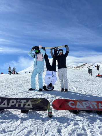 Karda kafa üstü duran kişi ve arkadaşları, ön planda CAPITA snowboard'lar.