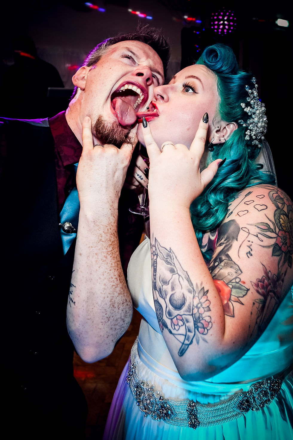 An alternative bride and groom with their tongues out making the rock on sign with their hands