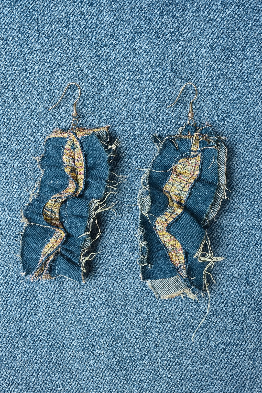 Two blue jean earrings, Denim Jean Earrings, laying on a denim background.