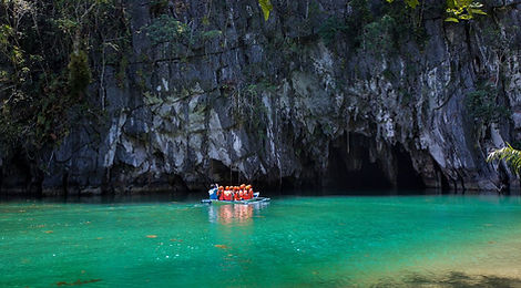 Tourists on a small boat enter the entrance of the UNESCO Puerto Princesa Underground River in Palawan, surrounded by massive cliffs and bright emerald water.