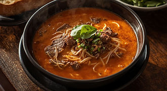 A steaming bowl of Chao Long, a famous Vietnamese-influenced beef noodle soup from Palawan, featuring tender beef strips and savory orange broth in a black bowl.