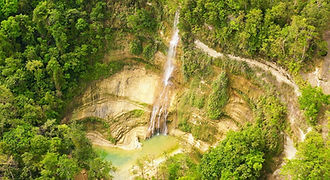 A dramatic aerial view of Can-umantad Falls in Candijay, Bohol, cascading down a high cliff into a natural turquoise pool surrounded by dense tropical forest.