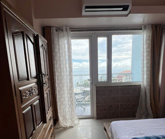 Bedroom interior inside Wind Residences Tower 1 showing a classic wooden wardrobe air conditioning and glass doors leading to a balcony overlooking Taal Lake