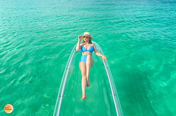 A professional photograph of a traveler in a blue swimsuit and straw hat relaxing in a transparent kayak over the vibrant turquoise waters of Boracay. The clear kayak offers an unobstructed view of the seafloor, representing a signature water immersion curated by Pearl Horizon Travel.