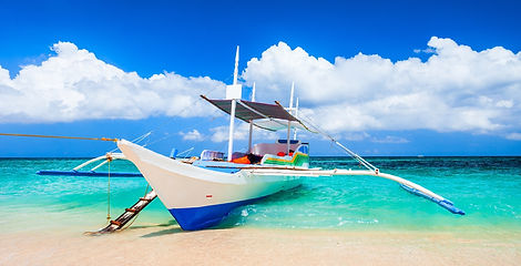Traditional paraw sailboats glide on peaceful sea waters as the golden sun sets over the horizon on White Beach in Boracay, Philippines.
