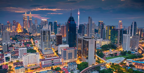 An aerial panorama of the Kuala Lumpur city skyline illuminated at dusk, featuring the Petronas Twin Towers and KL Tower in Malaysia.