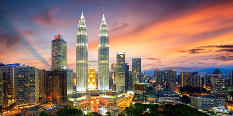 The twin spires of the Petronas Twin Towers rise above the Kuala Lumpur skyline under a dramatic orange and pink sunset sky in Malaysia.
