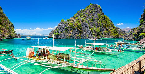 Traditional outrigger boats docked at a wooden boardwalk in the crystal-clear turquoise waters of Kayangan Lake entrance bay in Coron, Palawan.