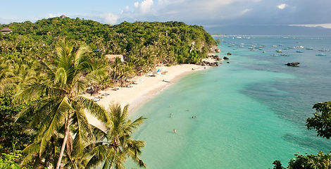 An aerial high-angle view of a serene white sand beach cove surrounded by lush palm trees and turquoise ocean water in Boracay, Philippines.