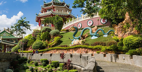 A green dragon sculpture lies on a manicured lawn below a traditional multi-tiered Chinese pagoda roof at the Cebu Taoist Temple in Cebu City.