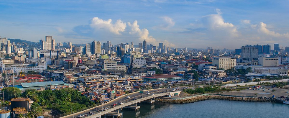 A wide high-angle view of the Cebu City urban skyline and coastal bridge in the Philippines, showcasing the modern city landscape and harbor under a clear blue sky.