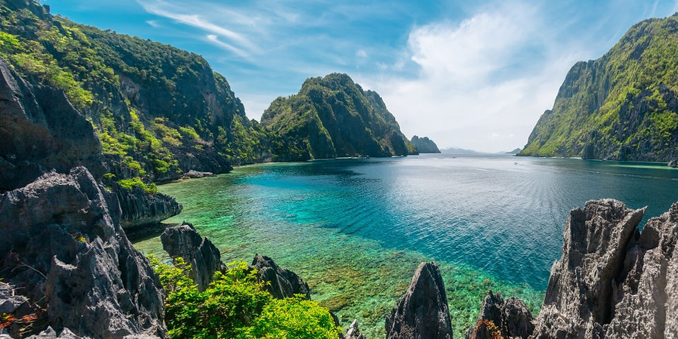 Towering dark limestone karst cliffs surround clear green and blue ocean waters along Tapiutan Strait off Matinloc Island in El Nido, Philippines.