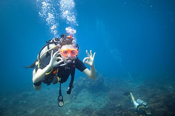 A scuba diver wearing an orange mask signals 'OK' while floating securely above the ocean floor during a guided dive in Boracay. Pearl Horizon Travel provides seamless reservations for these supervised introductory underwater descents.