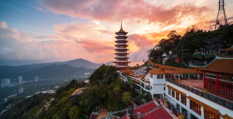 A tall nine-storey pagoda stands on a lush mountain ridge at Chin Swee Caves Temple in Genting Highlands, Malaysia, beneath a dramatic sunset sky.
