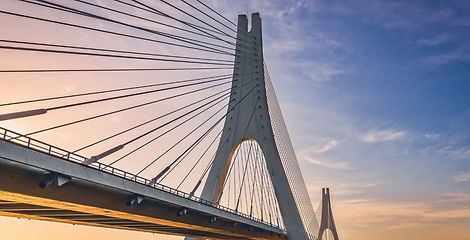 Looking up at the soaring towers and cable stays of the CCLEX bridge illuminated by soft sunset light against a blue sky in Cebu.