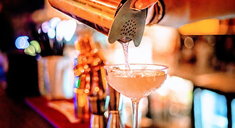 A professional bartender pours a clear, sparkling cocktail into a coupe glass, capturing the vibrant and sophisticated evening scene in a premium Cebu City lounge.