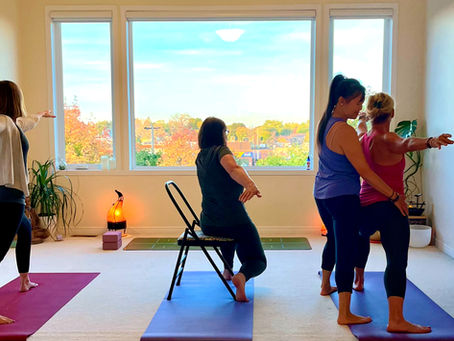 Nathaly guiding a gentle small-group yoga class in her Montreal studio, with students practicing standing and chair yoga.