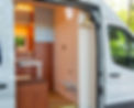 Custom Ford Transit camper van interior featuring light blue and dark wood accents, and partition wall behind driver’s cab by Redpoint Vanture
