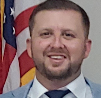 Todd Payne Smiling in suit, American flag behind him
