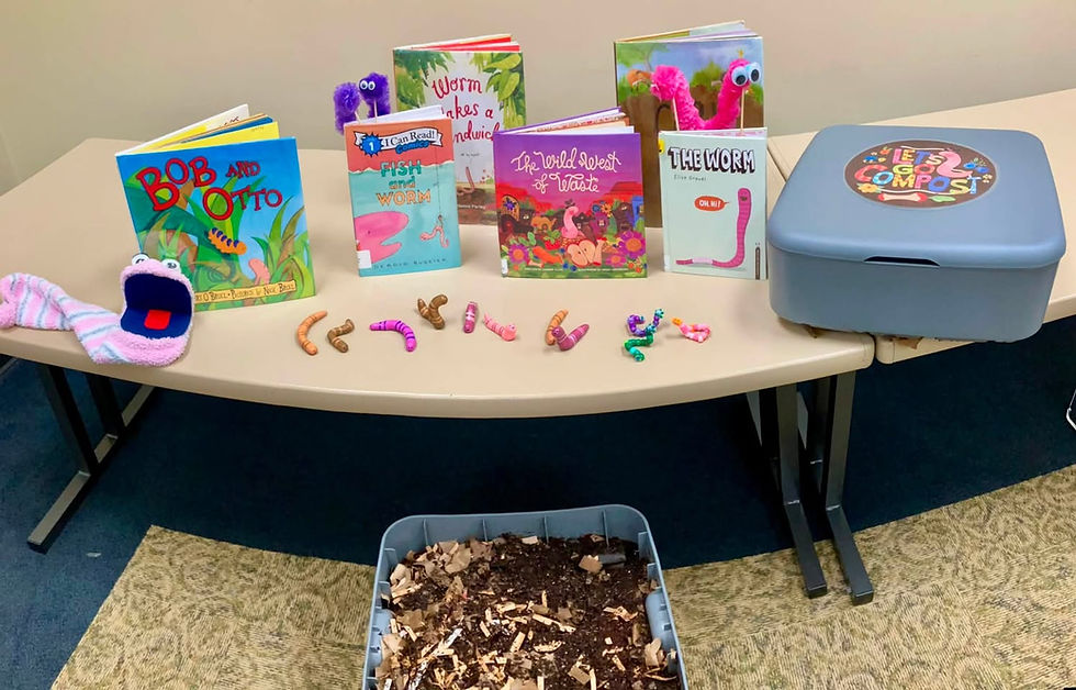 Worm-themed classroom display with childrens books, toy worms, and a compost bin labeled Lets Go Compost on a table.