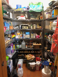 An image of a large and cluttered pantry. There are potatoes and jugs of water on the floor.