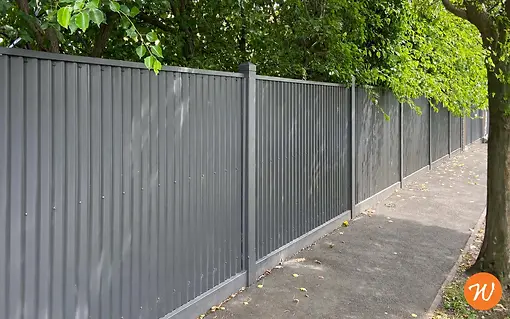 corrugated_fence_beneath_dappled_trees.webp