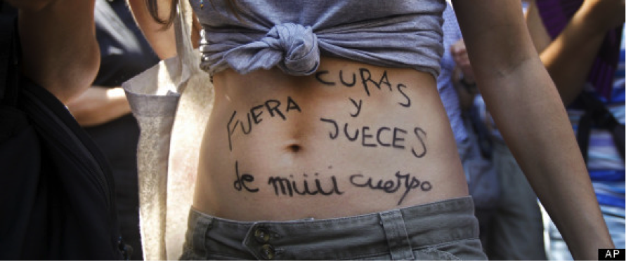 A young woman protesting against plans to again restrict abortion access, in Madrid in 2012. She has tied her t-shirt in a knot just under her chest and written the slogan “Judges and priests away from my body” in Spanish on her belly, emphasis on the “my.” Image Credit: AP Photo/Andres Kudacki