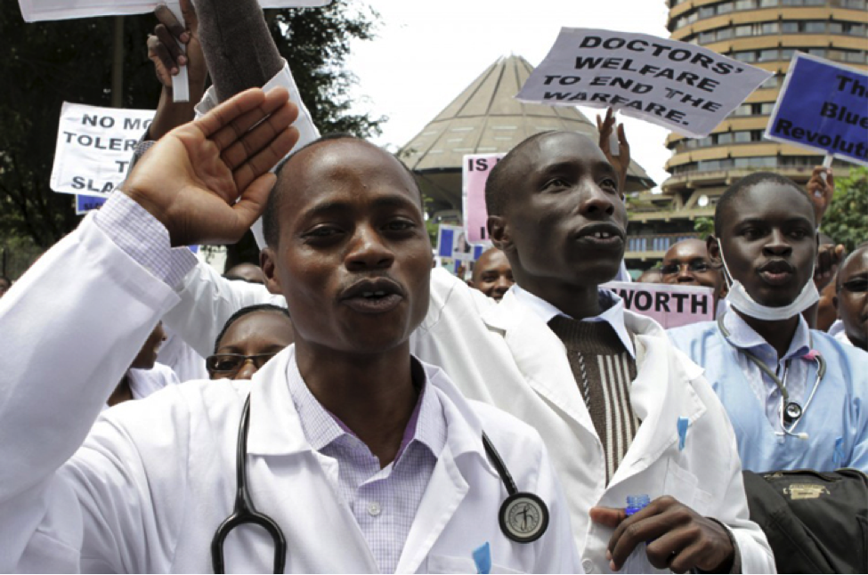 IMAGE DESCRIPTION: On March 1 of 2012, doctors in Kenya went on strike to protest the government’s failure to increase their pay. This image shows a crowd of Kenyan physicians with stethoscopes draped around their necks, some wearing surgical masks, most wearing white coats and some with surgical gowns. They have blue ribbons pinned to the chest pockets on their white coats. Protest signs are visible behind the first rank of protesters, bearing messages such as “Doctors’ welfare to end the warfare” and “The blue revolution.” Other slogans can be seen partially but cannot be discerned in entirety, including the word “worth.” The strike lasted two weeks, during which time the Kenyan government decided to fire the 25,000 health workers who refused a return-to-work order issued after the first week of work stoppage. One condition of stopping the strike was that the government rescind this decision. Another was that workers’ “extraneous allowances” would be increased by 100 per cent (doubled); this is not the same as their salary. The strike “paralysed operations in all of Kenya’s public hospitals.” Both doctors and nurses participated. Another cause of the protest in addition to salary was a demand for improved resources and services in the country’s most ill-equipped public hospitals. IMAGE CREDIT: Reuters