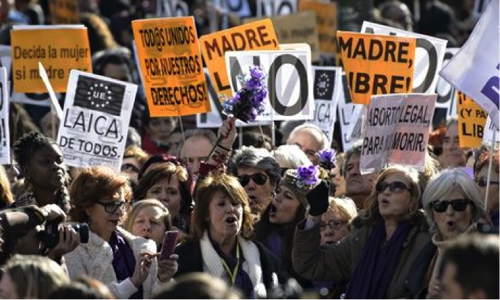 Demonstrators in favor of increased abortion access from across Spain wave signs in Madrid. One reads “todos unidos por nuestros derechos” (“all united for our rights”) and others bear a common slogan seen at these protests, “Madre, Libre!” (roughly: “mother, be free!”). Another common slogan: “Laica, de todos” (roughly: “Secularism, for all”), rejecting the imposition of a particular religious morality through law. Image Credit: Dani Pozo/AFP/Getty Images