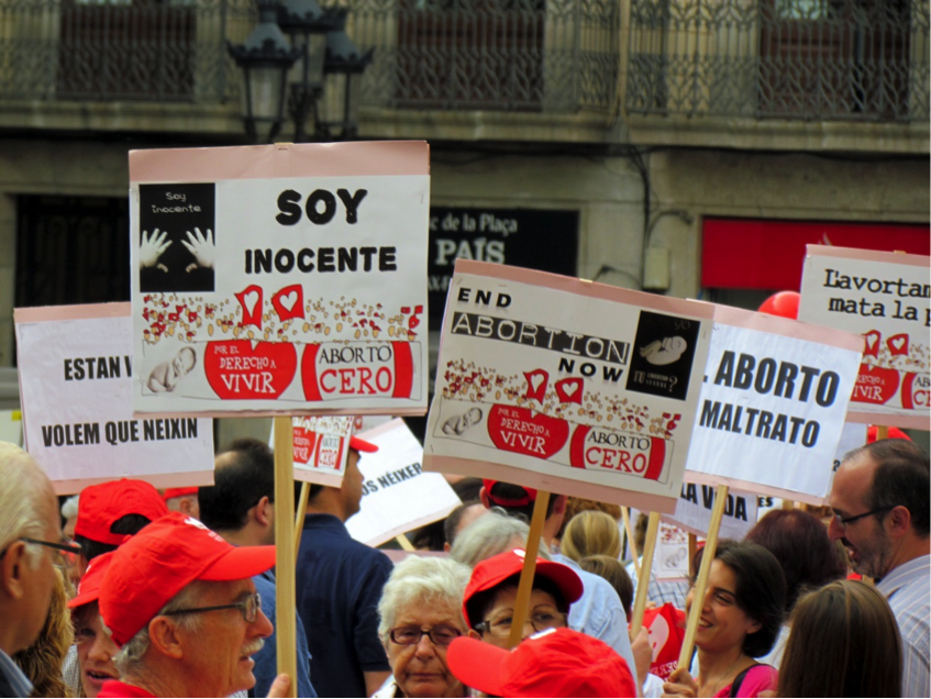 An October 2012 pro-life protest in Barcelona, Spain with signs in both Spanish and English (perhaps for the foreign press). Slogans read “aborta cero” (roughly: zero abortions) and signs show an image of a child’s hands with the message “soy innocente” (“I am innocent”). The protesters are against a 2010 expansion of abortion access in Spain. Many of the people in the image, both men and women, are older and have white hair. Others are younger and have dark hair. Image Credit: David Berkowitz.