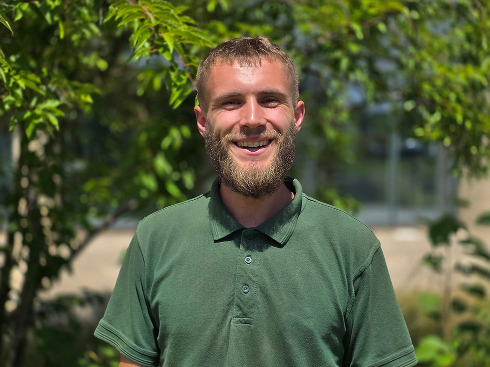 Grounds maintenance operative wearing green polo and smiling in front of green landscape