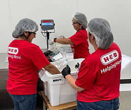 Volunteers in red H-E-B shirts packing items into bins.