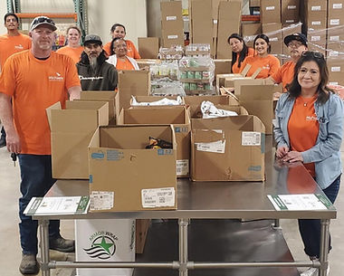 Volunteers in orange shirts standing behind boxes in a warehouse.