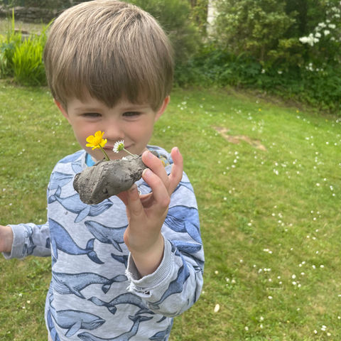 Boy playing with stones and flowers outside at Rodborough Playgroup