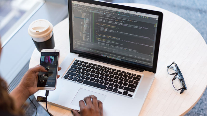 Una persona lavora con computer e cellulare, simboli dei vantaggi e svantaggi della tecnologia