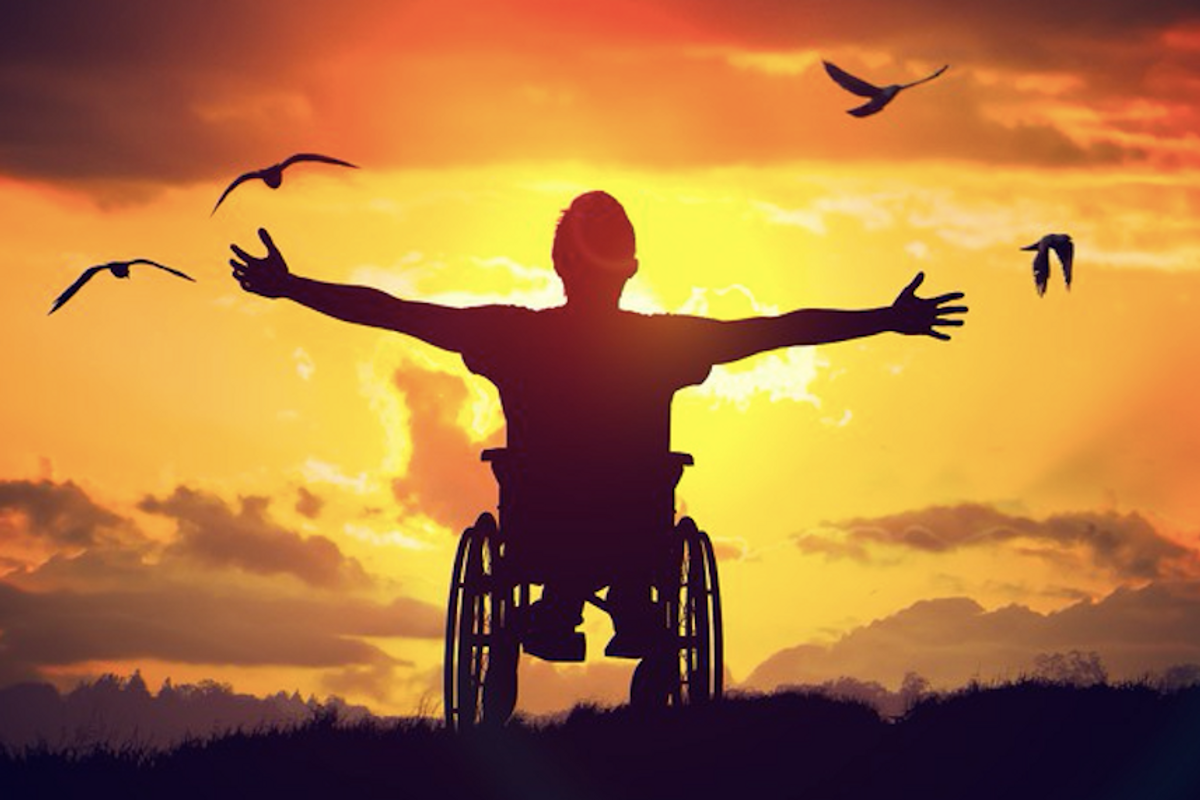 Persona di spalle su sedia a rotelle su un prato che guarda il tramonto con le braccia aperte