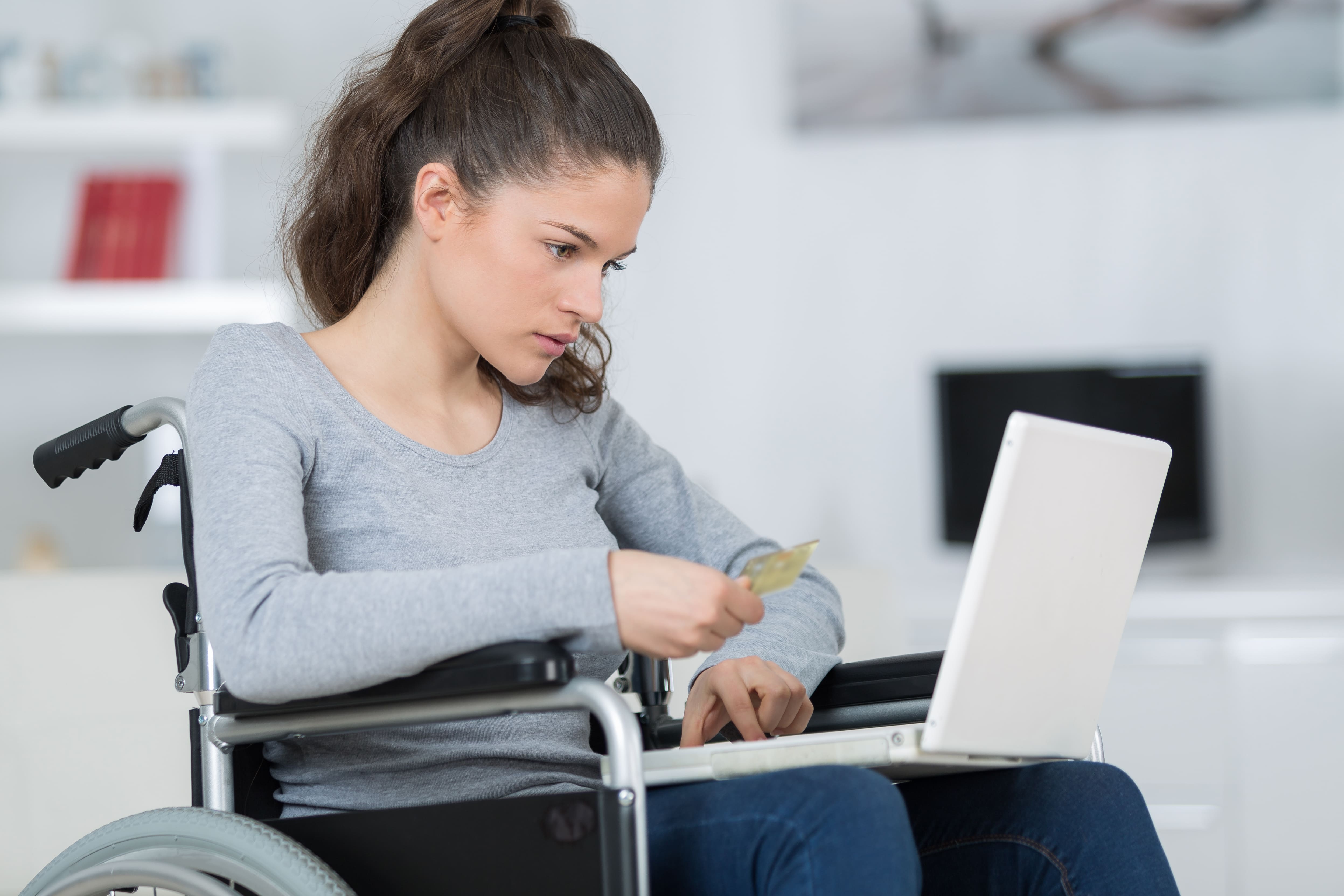 Una ragazza con disabilità motoria agita una arta di credito di fronte a un pc